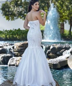 Woman in a strapless white mermaid gown stands by a pond with a fountain, facing away from the camera.