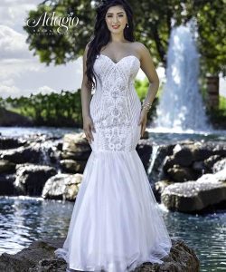 Woman in a strapless white mermaid gown stands on rocks by a pond with a fountain in the background.