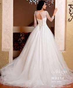 A woman in an ivory white, long-sleeve ball gown wedding dress stands facing away, showing a lace-up back.