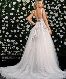 Woman wearing a beaded applique tulle gown with a low back, standing before a flower-covered wall.