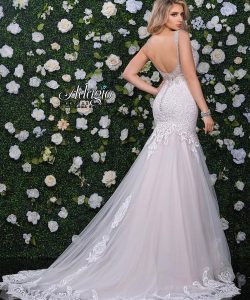 A woman in a white lace-back mermaid wedding dress stands in front of a green wall with white flowers.