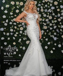Woman in a fitted, ivory-white beaded applique tulle gown poses in front of a flower-covered wall backdrop.