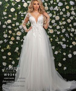 Woman in a white wedding gown with floral appliqués stands in front of a green wall decorated with white roses.