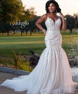 A woman stands outdoors wearing a white lace mermaid wedding dress with a fitted bodice and a flared tulle skirt.