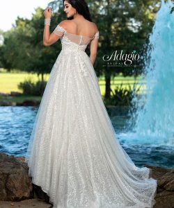 Woman in an off-the-shoulder white bridal gown stands near a fountain in a park, facing away from the camera.