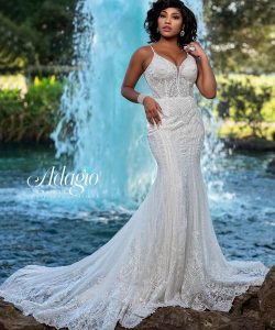 A woman in a fitted, lace mermaid wedding gown stands by a pond with a waterfall in the background.