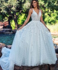 A woman stands outdoors in a lace-embellished, sleeveless ballgown wedding dress with a full tulle skirt and train.