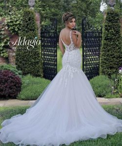 Woman in a white lace wedding dress stands outdoors in front of black wrought iron garden gates, looking over her shoulder.