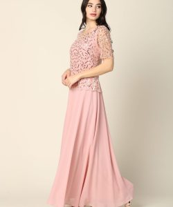 Woman wearing a light pink, floor-length dress with a patterned lace top and short sleeves, standing against a plain background.