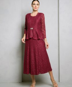 Woman wearing a burgundy lace three-piece dress with long sleeves, standing against a plain gray wall.